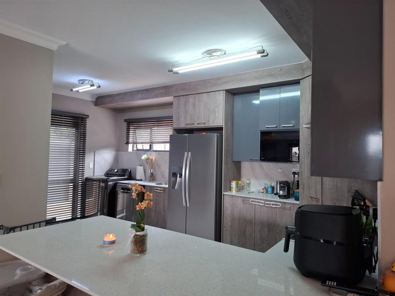 Modern kitchen featuring a stone-topped breakfast island, sleek grey cabinetry, integrated storage, and contemporary lighting fixtures.