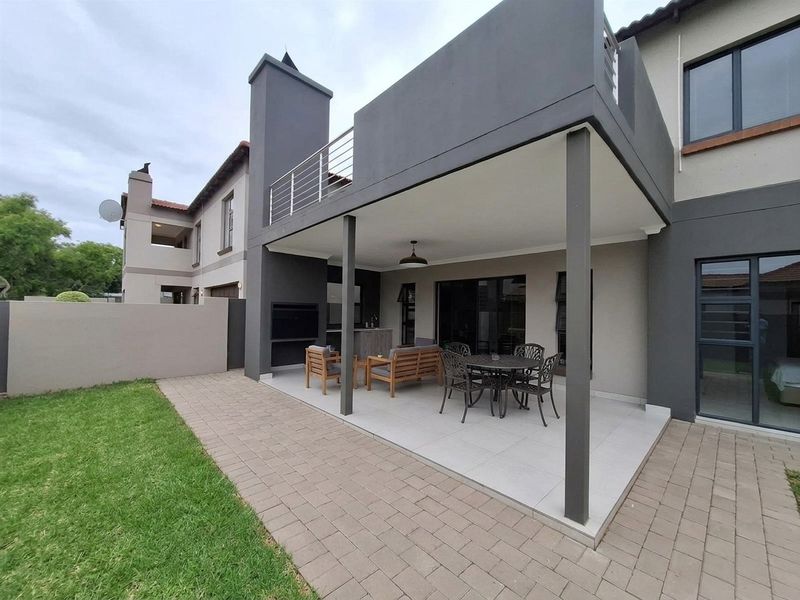 A covered patio area featuring a built-in braai, tiled flooring, and direct access to the rear garden and upper-level balcony.