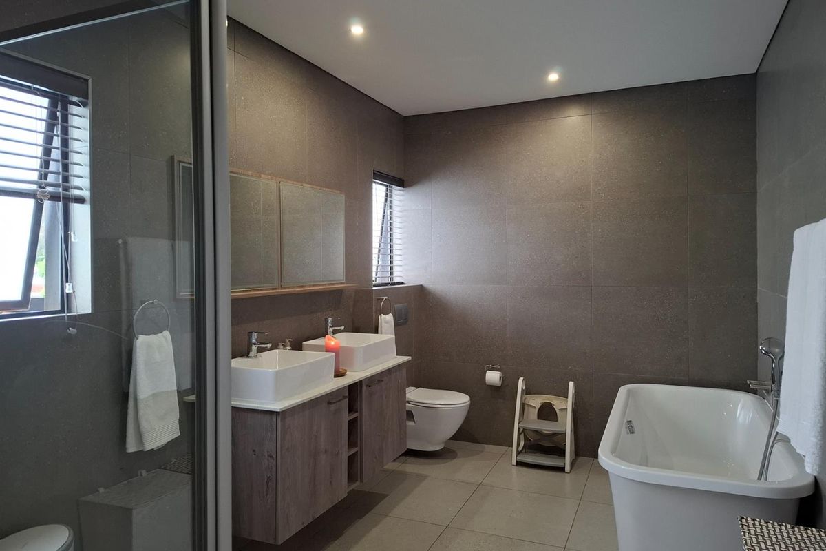 Modern bathroom featuring a double vanity with vessel sinks, a freestanding bathtub, a glass-enclosed shower, and large-format floor-to-ceiling wall tiles.