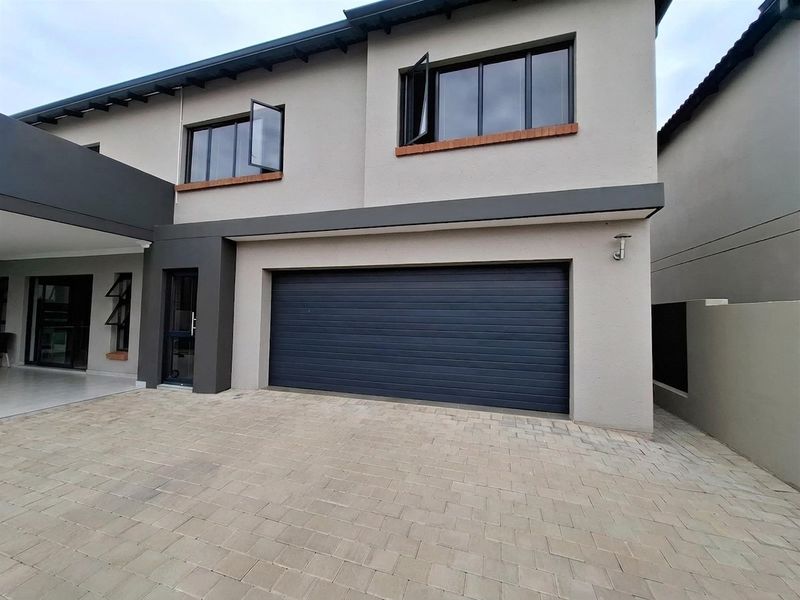 Modern double-story residential facade featuring a paved driveway, integrated garage, and contemporary window frames.