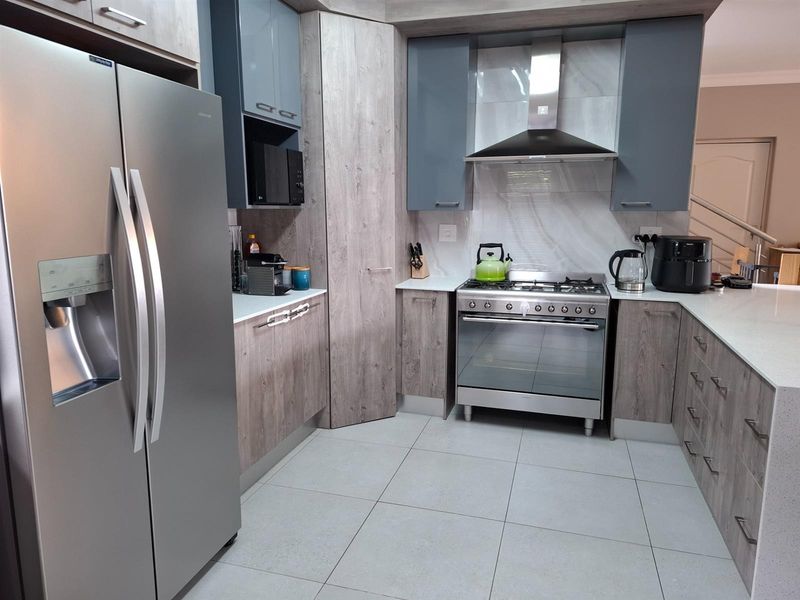 Modern kitchen featuring two-tone cabinetry, stone-look countertops, tiled flooring, and a stainless steel gas stove with a matching extractor fan.