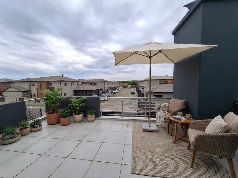 A spacious elevated balcony featuring modern tiled flooring and stainless steel railings, offering an open view of the surrounding residential estate.