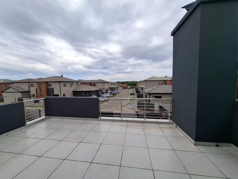 A spacious upper-level balcony featuring modern tiled flooring and stainless steel railings, offering an elevated view of the surrounding residential estate.