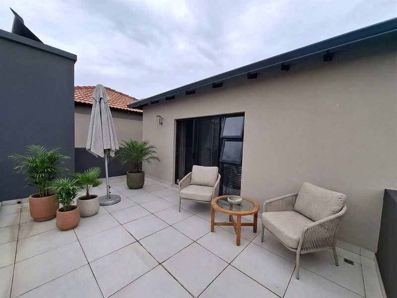 A well-maintained outdoor patio area featuring modern light-colored floor tiles and direct access to the interior through sliding glass doors.