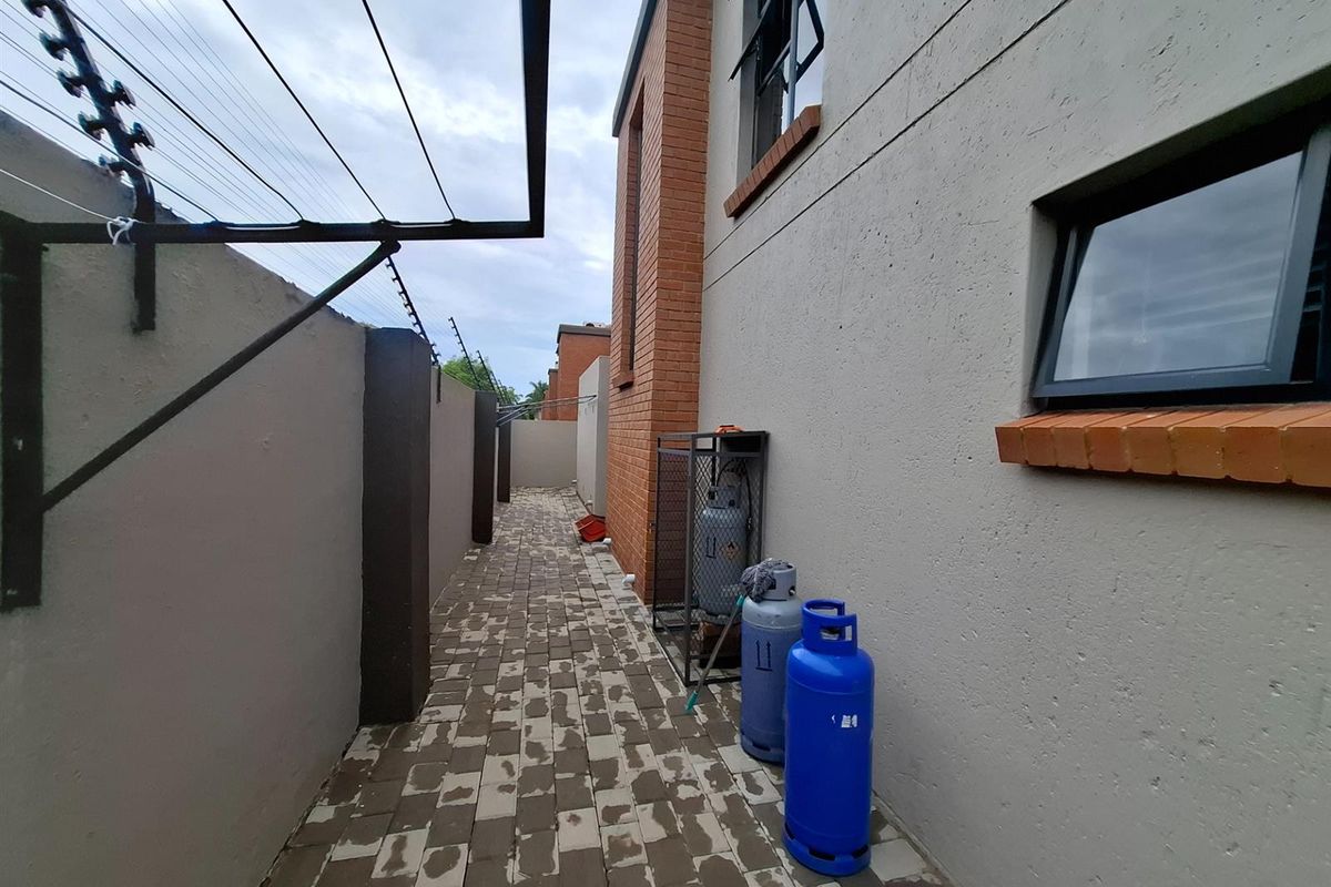Side exterior walkway featuring paved flooring, brick detailing, and perimeter security fencing.