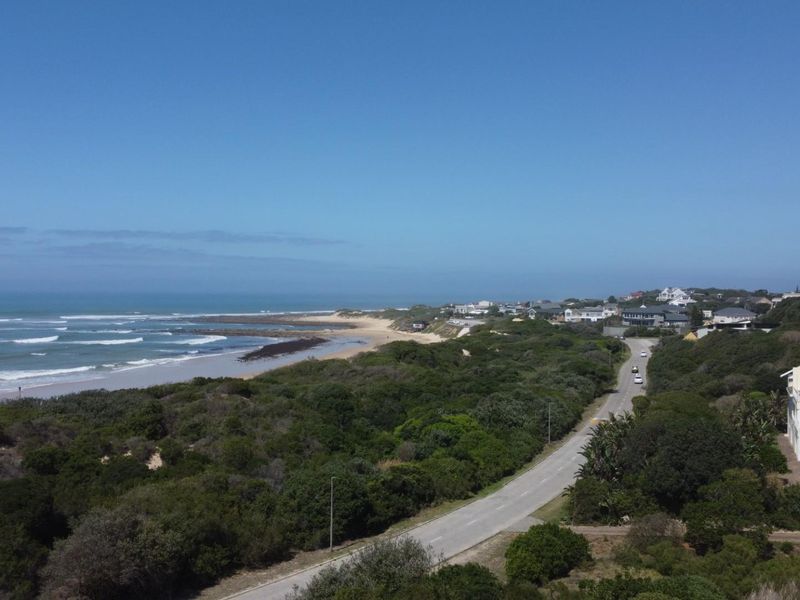 Aerial view of the coastal landscape, featuring a scenic beach, surrounding vegetation, and nearby residential properties along the road.