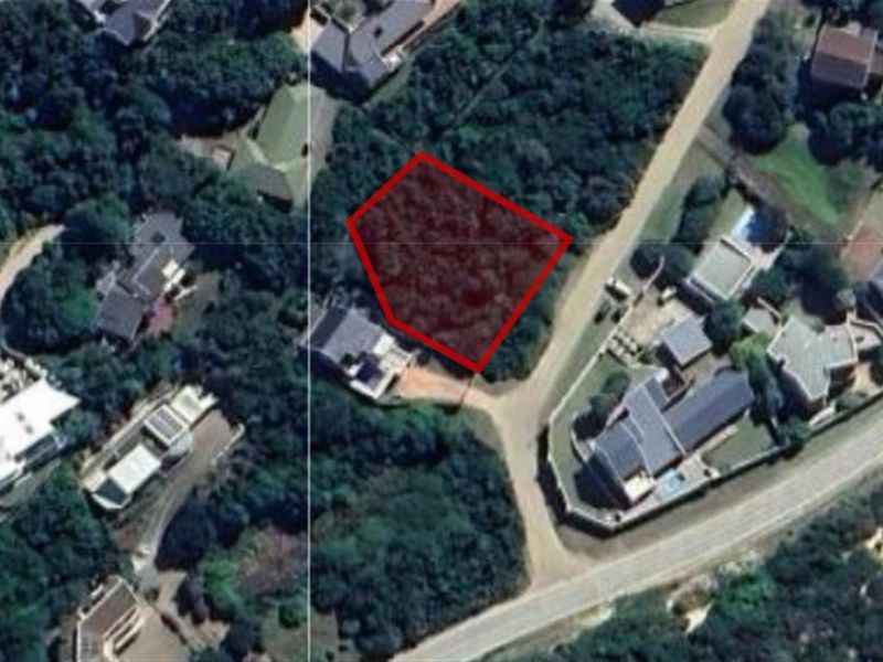 An aerial view of a vacant residential plot highlighted in red, situated within a developed neighborhood with established vegetation.