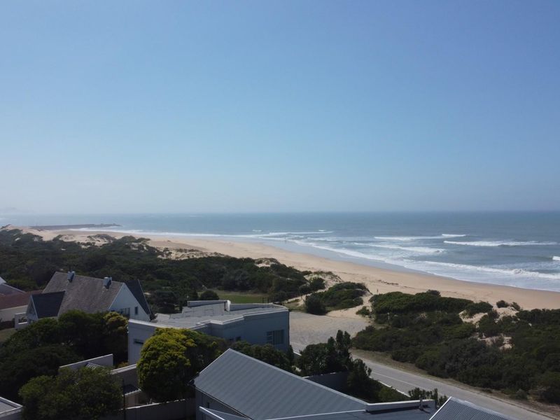 An elevated aerial view showcasing the coastal landscape, sandy beach, and surrounding residential properties in a scenic seaside setting.