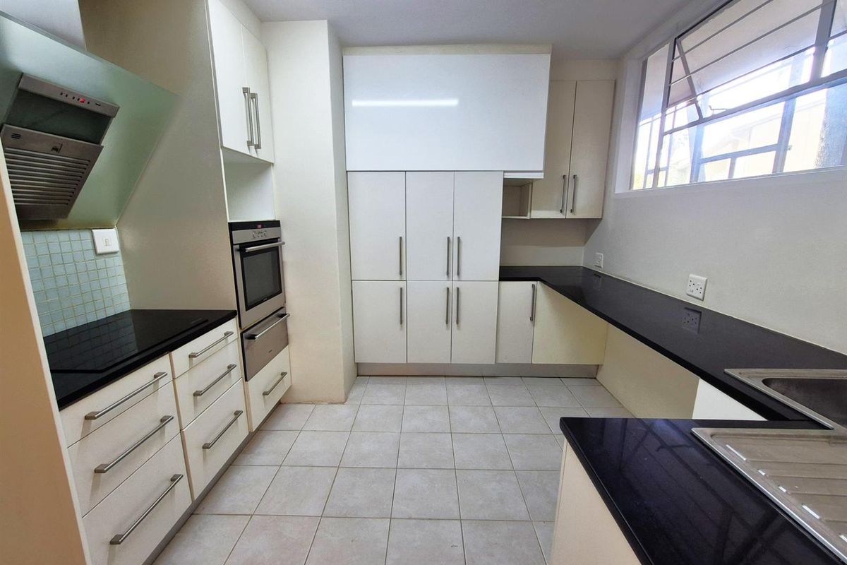 A well-maintained kitchen featuring modern white cabinetry, contrasting black countertops, a built-in oven, and an extractor fan.