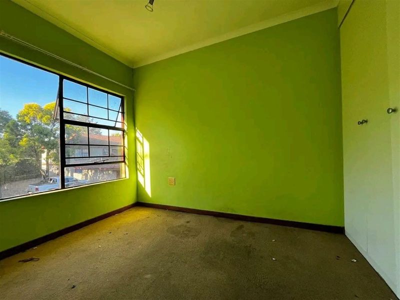 An empty bedroom featuring a large steel-framed window, built-in cupboard, and carpeted flooring, requiring cosmetic updates to the walls and flooring.