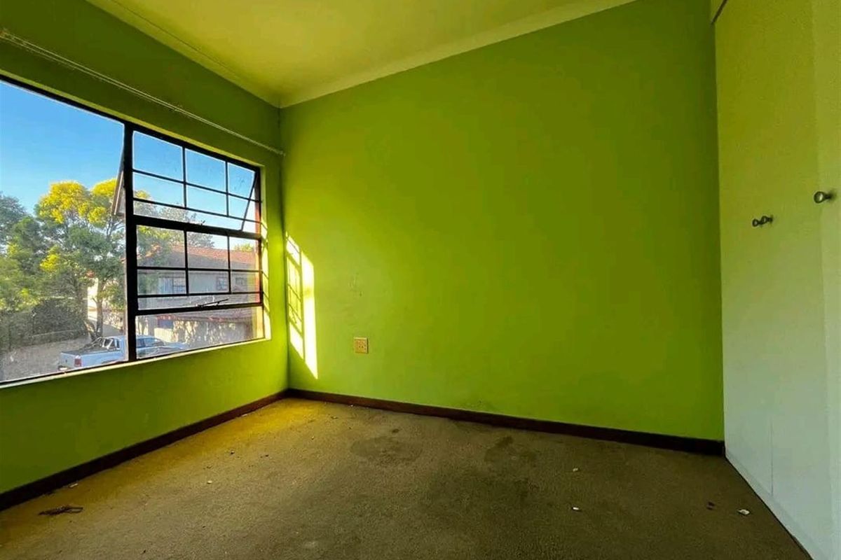 An empty bedroom featuring a large steel-framed window, built-in cupboard, and carpeted flooring, requiring cosmetic updates to the walls and flooring.