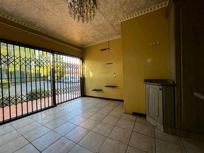 An empty living area featuring tiled flooring, a textured ceiling, built-in cabinetry with granite countertops, and a security gate leading to the exterior.
