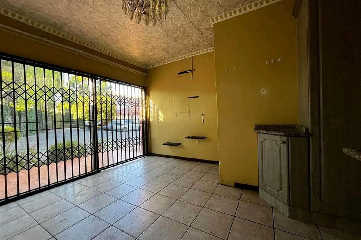 An empty living area featuring tiled flooring, a textured ceiling, built-in cabinetry with granite countertops, and a security gate leading to the exterior.