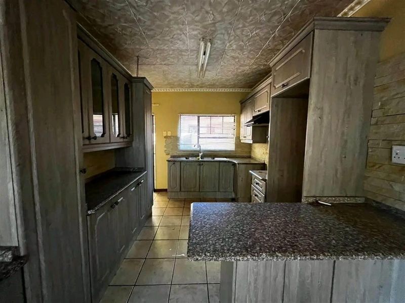 A dated kitchen featuring built-in cabinetry, granite countertops, and tiled flooring, offering a functional layout ready for modernization and cosmetic updates.