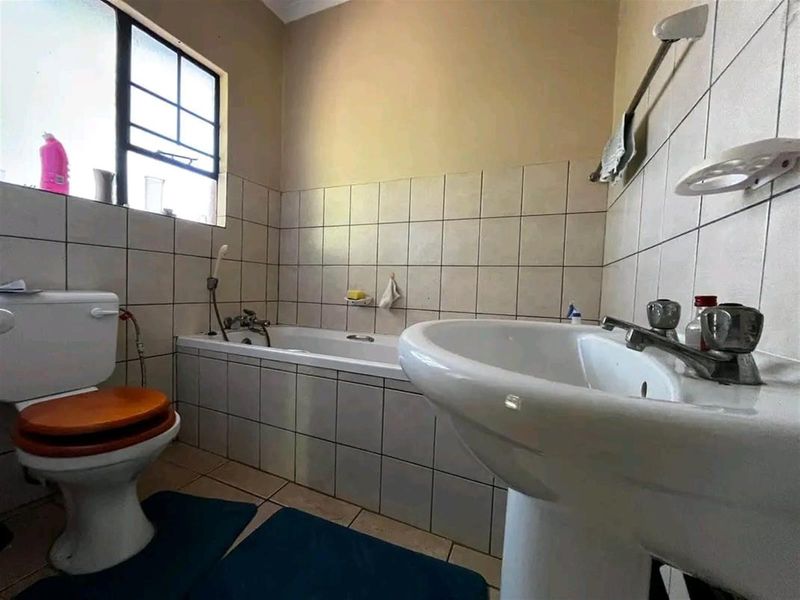 A functional bathroom featuring a pedestal basin, bathtub, and toilet with neutral wall and floor tiling.