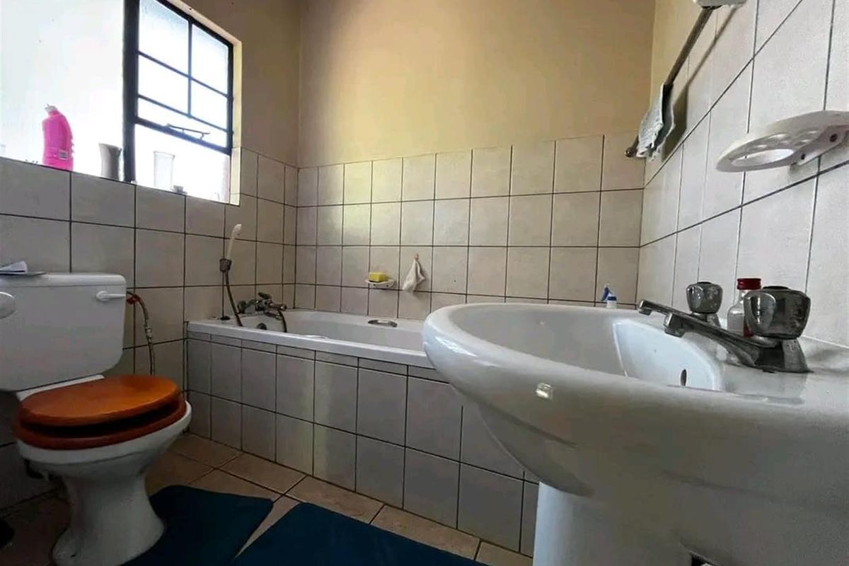A functional bathroom featuring a pedestal basin, bathtub, and toilet with neutral wall and floor tiling.