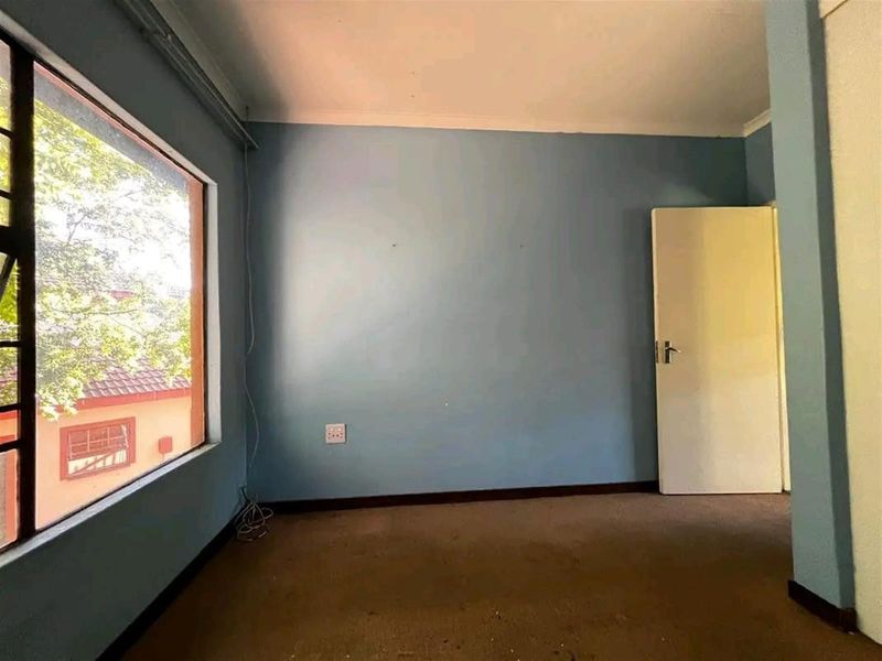 An empty bedroom featuring a large window, carpeted flooring, and blue painted walls, offering a blank canvas for potential renovation or staging.