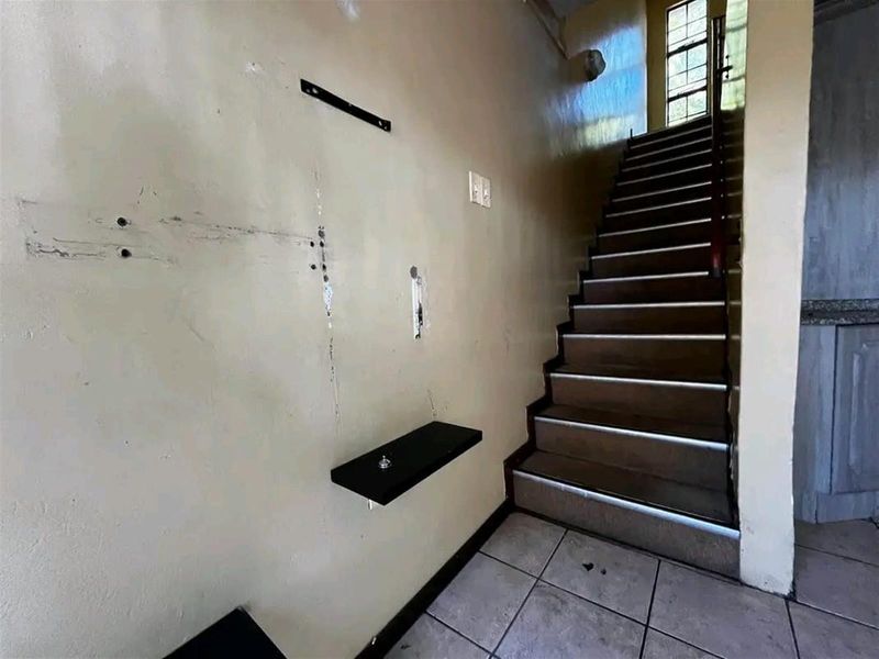 A hallway featuring a staircase with tiled flooring and visible wall damage requiring cosmetic repair and repainting.