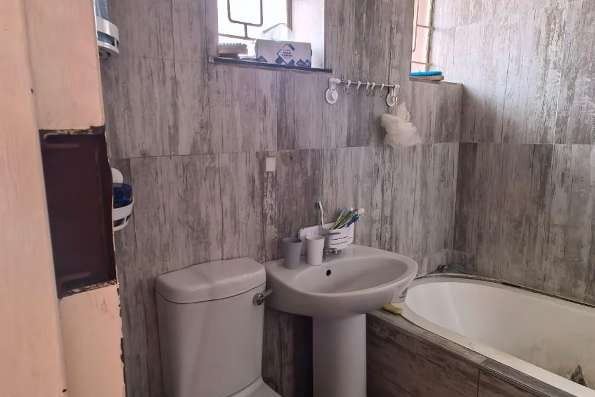 A compact bathroom featuring a pedestal sink, toilet, and built-in bathtub with grey wood-look wall and floor tiling.