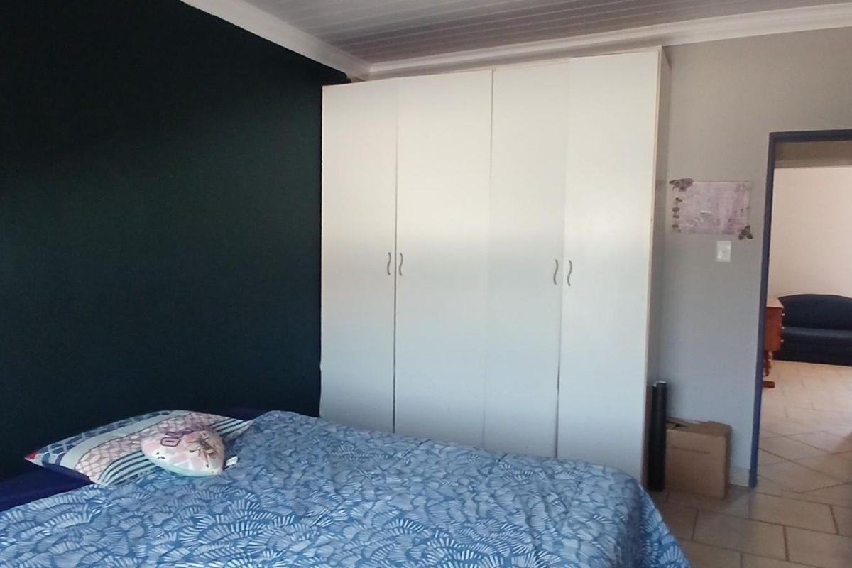 A bedroom featuring built-in white wardrobes, tiled flooring, and a dark accent wall, with an adjacent view into a hallway.