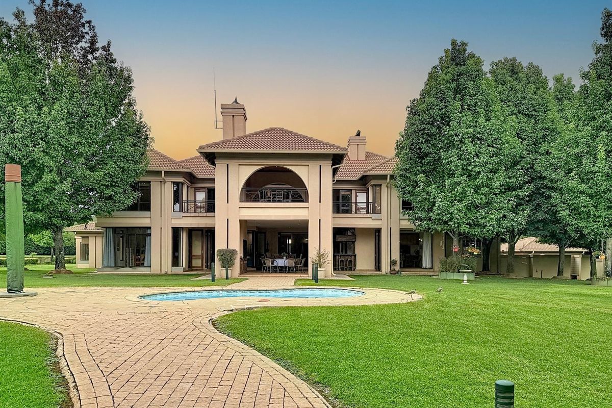 A spacious rear exterior view of a large multi-story residence featuring a swimming pool, paved walkway, and expansive landscaped garden.