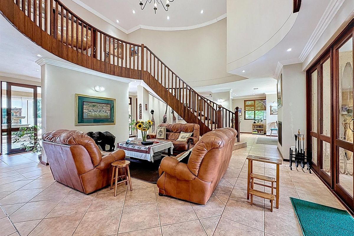 Spacious living area featuring a grand curved wooden staircase, tiled flooring, and high ceilings with recessed lighting, creating an open and inviting atmosphere.