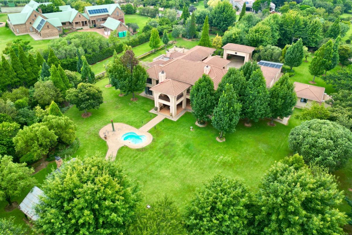Aerial view of a large residential property featuring a tiled roof, swimming pool, expansive landscaped gardens, and multiple outbuildings.