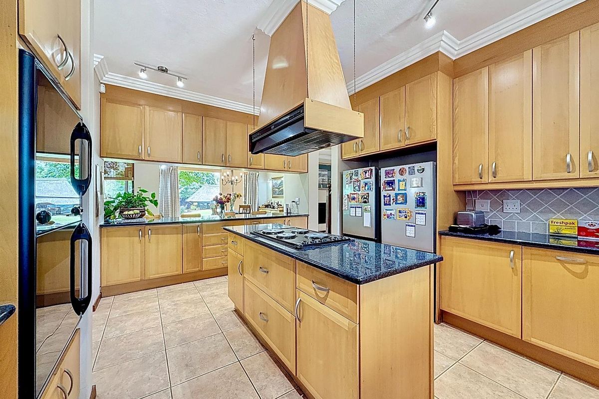A functional kitchen featuring light wood cabinetry, granite countertops, a central island with a built-in hob, and a suspended extractor fan.
