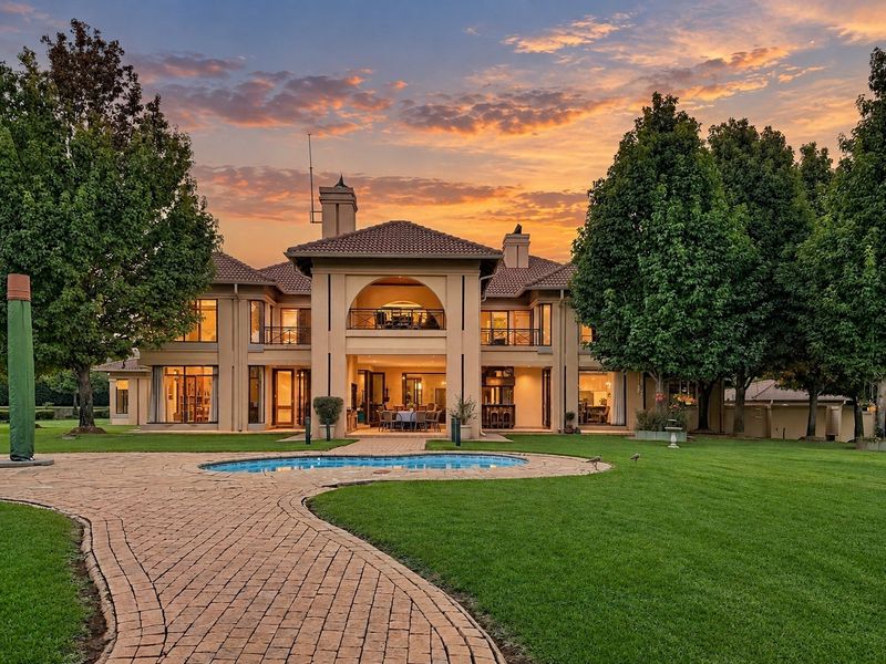 A stunning rear view of a luxury residence featuring a manicured garden, paved walkway, swimming pool, and a spacious covered balcony at sunset.
