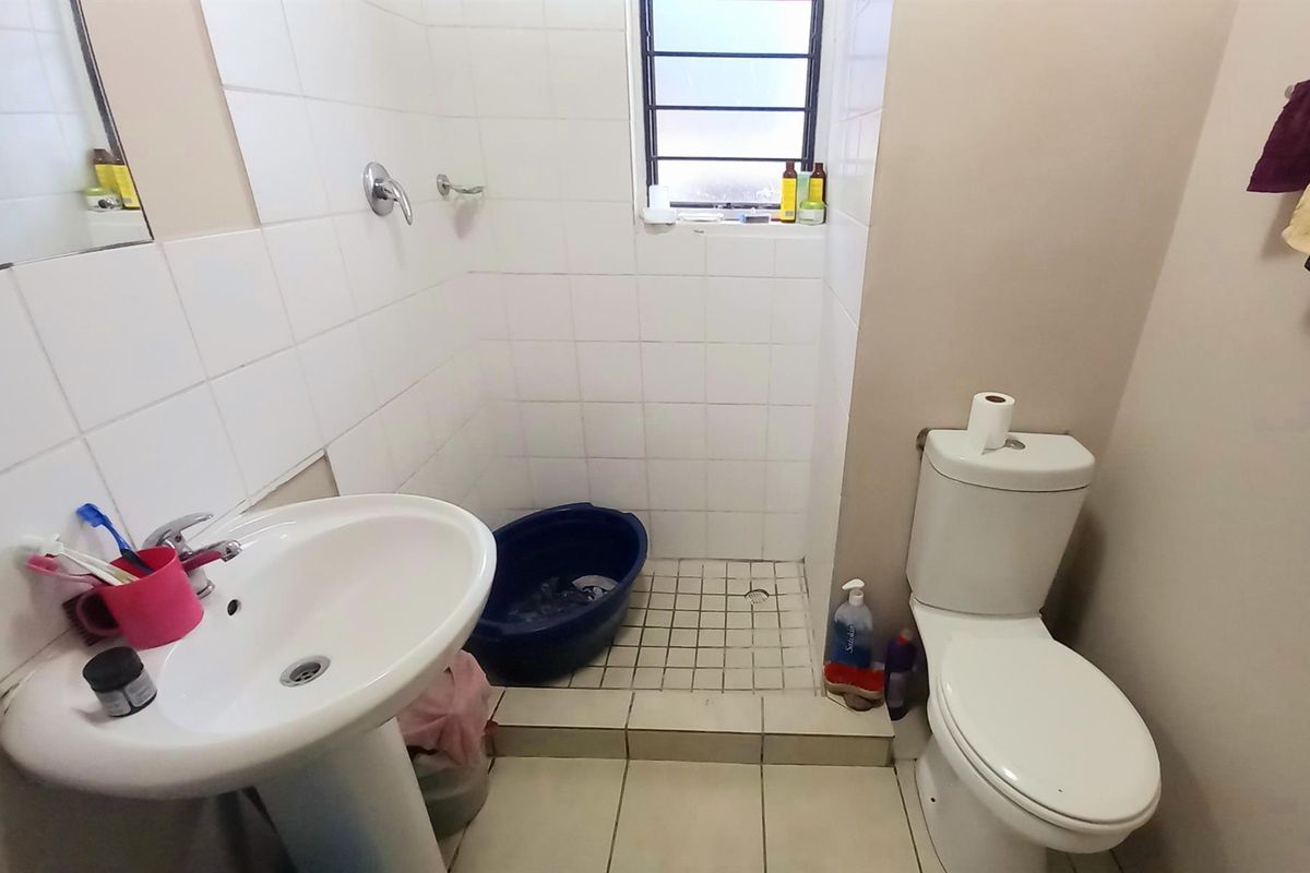 A functional bathroom featuring a pedestal basin, a tiled shower enclosure with a window, and a standard toilet.