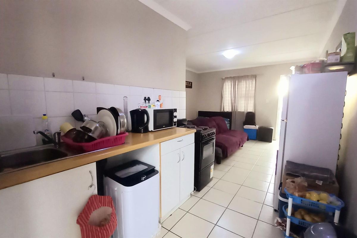An open-plan apartment layout featuring a functional kitchen area with built-in cabinetry and a stove, flowing into a living space with tiled flooring.