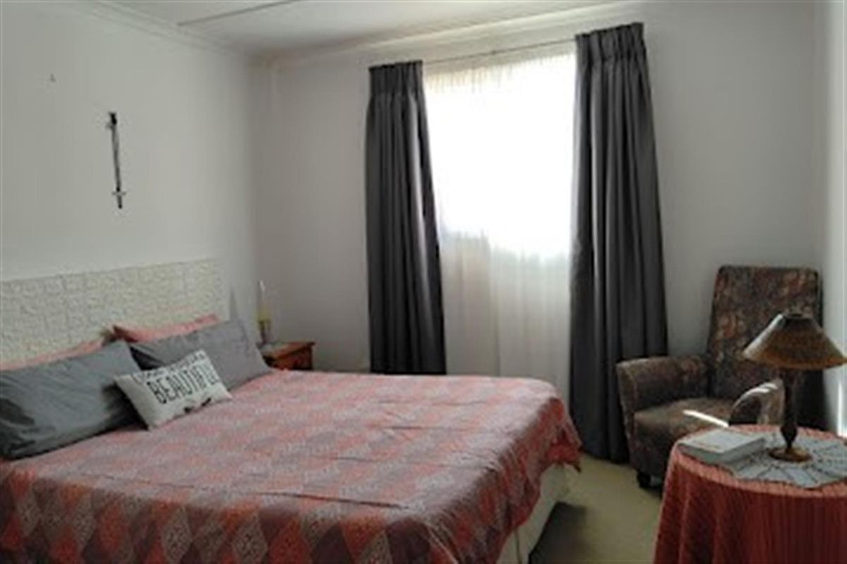 A standard bedroom featuring neutral walls, carpeted flooring, and a window dressed with floor-length curtains.