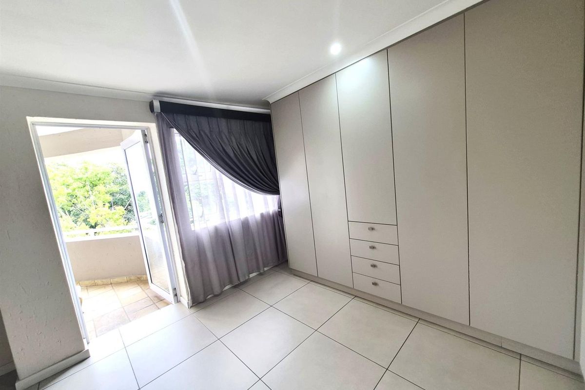 A bright bedroom featuring large built-in cupboards, tiled flooring, and direct access to a private balcony through a glass door.