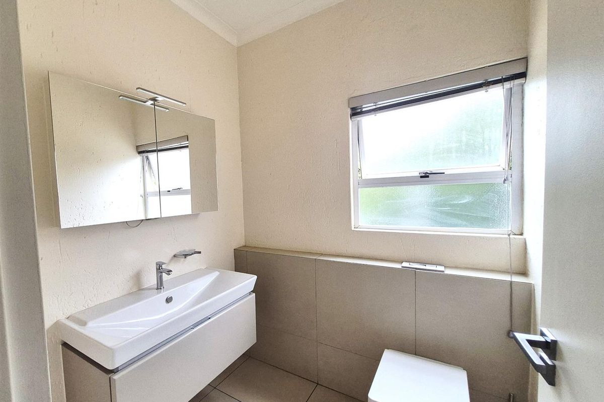 A functional bathroom featuring a wall-mounted vanity with integrated basin, a modern toilet, and a window with fitted blinds.