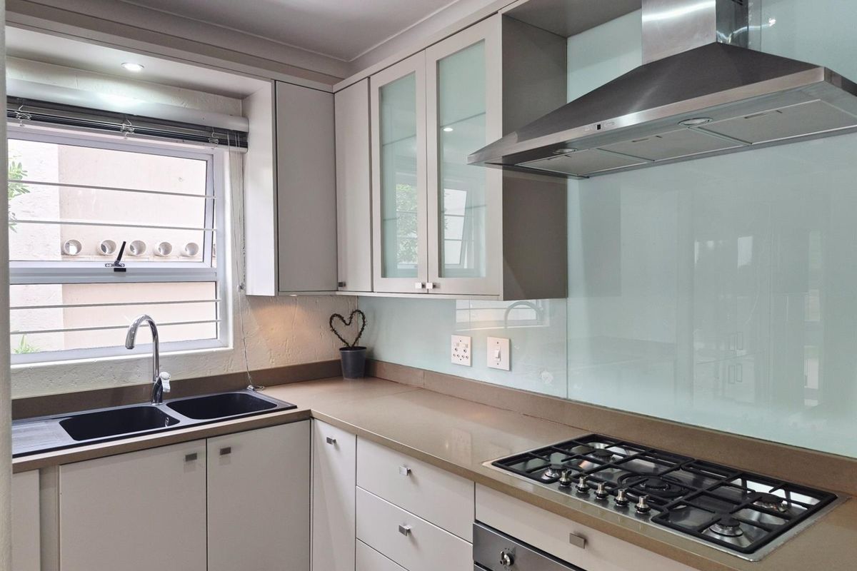 Modern kitchen featuring light-toned cabinetry, stone countertops, a glass splashback, a built-in gas hob, stainless steel extractor fan, and a double-basin sink.