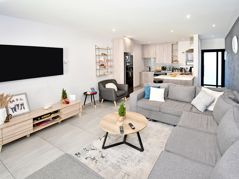 A modern open-plan living and kitchen area featuring neutral tiled floors, contemporary cabinetry, a kitchen island, and recessed lighting throughout the space.