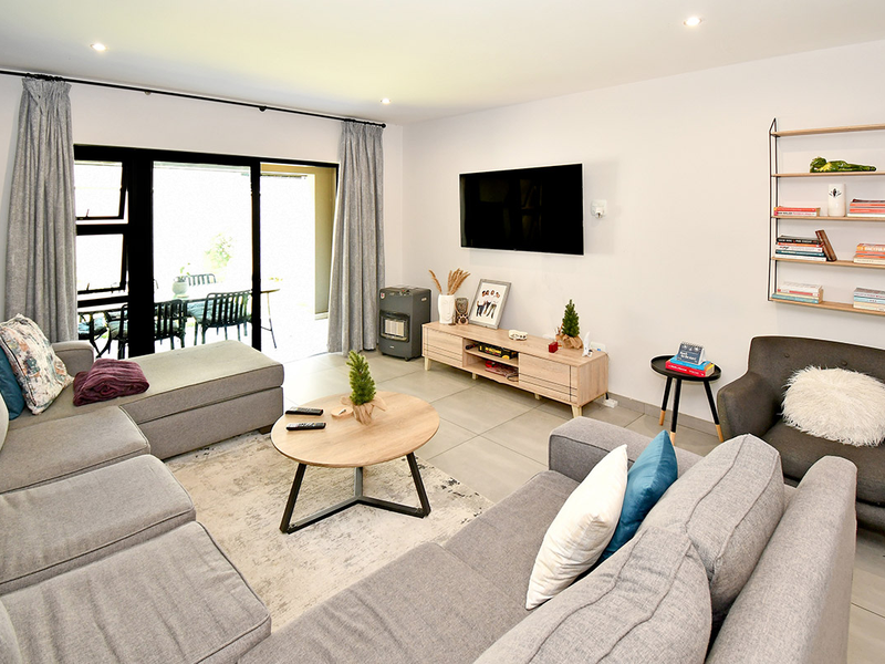 A bright and modern living room featuring large sliding glass doors that open to an outdoor patio area, complemented by neutral tiled flooring.