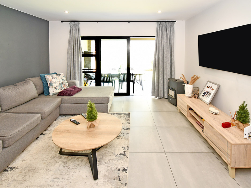 A bright and modern living room featuring large format floor tiles, a feature accent wall, and sliding glass doors leading to an outdoor patio area.