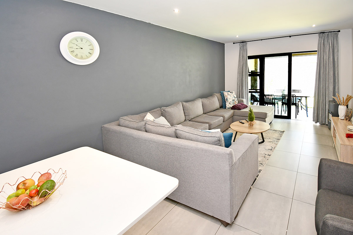 A bright and modern living room featuring large format floor tiles, recessed downlighting, and sliding glass doors providing access to the patio area.