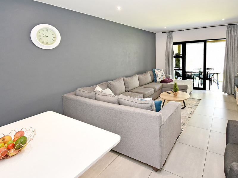 A bright and modern living room featuring large format floor tiles, recessed downlighting, and sliding glass doors providing access to the patio area.