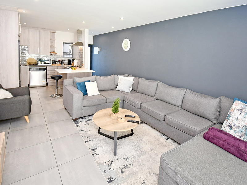 Modern open-plan living area featuring a contemporary kitchen with built-in cabinetry and a central island, seamlessly flowing into a spacious lounge with tiled flooring.