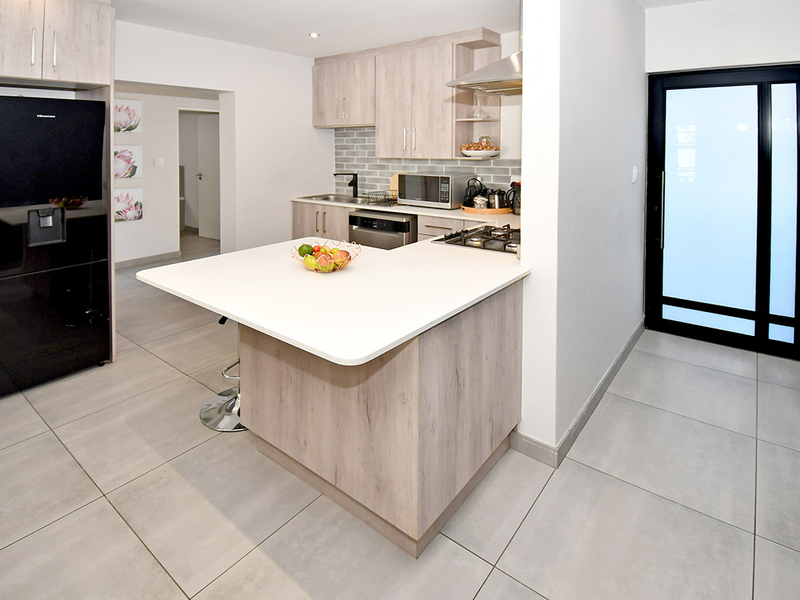Modern kitchen featuring light wood cabinetry, a central island with a breakfast bar, gas hob, extractor fan, and neutral tiled flooring.