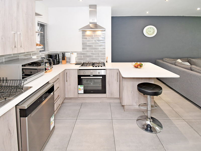 Modern open-plan kitchen featuring light wood cabinetry, stone countertops, stainless steel appliances, and a breakfast bar, seamlessly flowing into the living area.