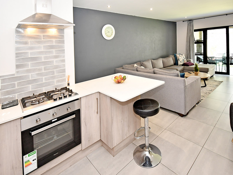 Modern open-plan kitchen and living area featuring a gas cooktop, stone countertops, tiled flooring, and direct access to an outdoor patio through sliding doors.