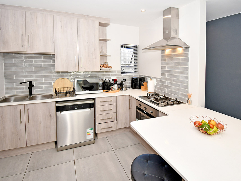 Modern kitchen featuring light wood-grain cabinetry, quartz countertops, subway tile backsplash, stainless steel appliances, and a functional breakfast bar layout.