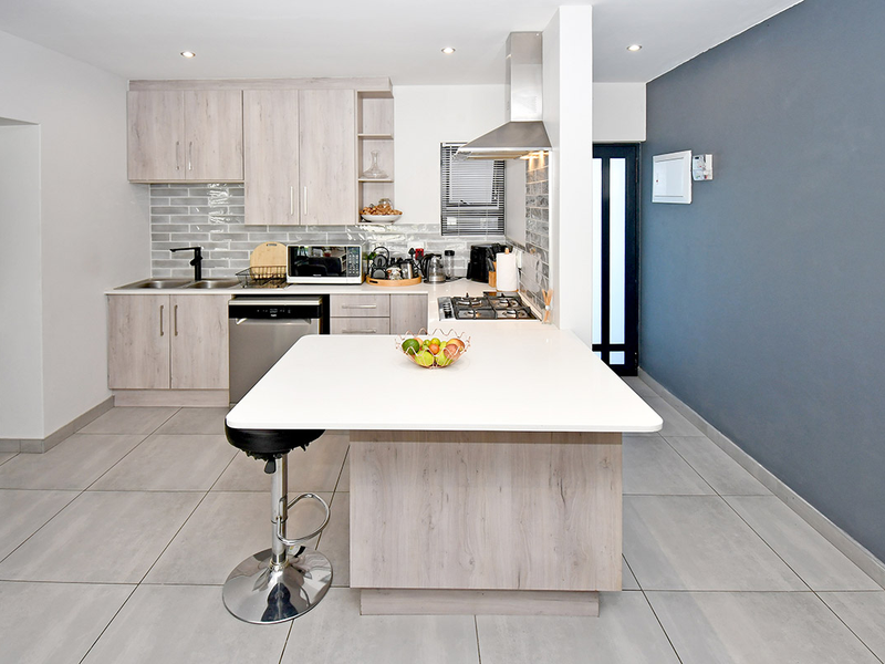 Modern kitchen featuring light wood-grain cabinetry, stone countertops, a central island with breakfast bar, gas hob, and stylish subway tile backsplash.