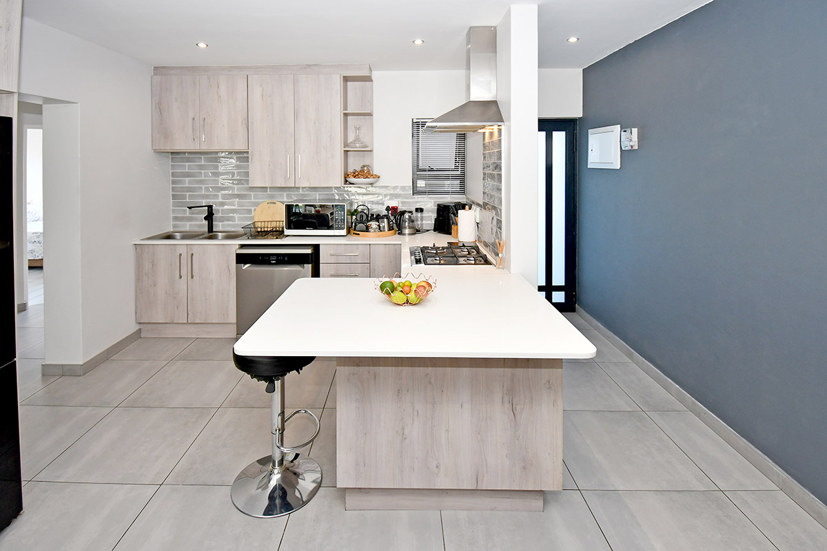Modern kitchen featuring light wood-grain cabinetry, stone countertops, a central island with breakfast bar, gas hob, and stylish subway tile backsplash.