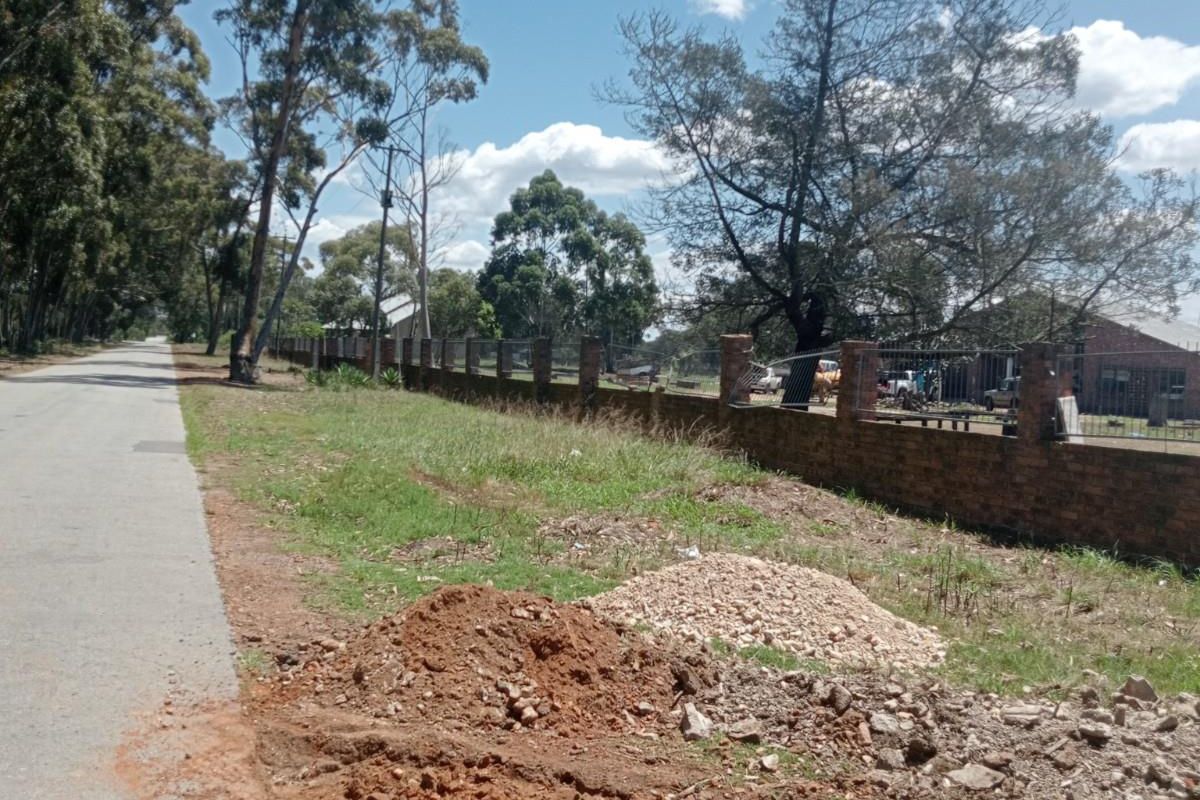 A street-level view of the property boundary featuring a brick perimeter wall and adjacent road access.
