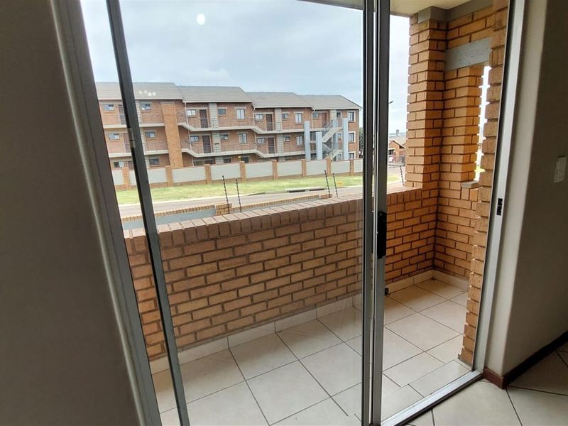 A covered balcony featuring a brick balustrade, tiled flooring, and a sliding glass door, offering an outdoor space for relaxation.