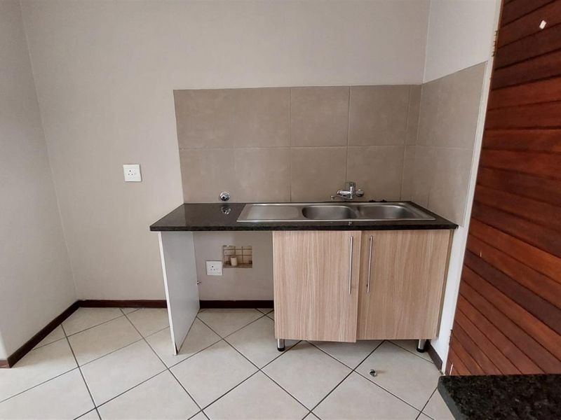 A functional scullery area featuring a double bowl stainless steel sink, granite countertops, tiled splashback, and under-counter cabinetry.